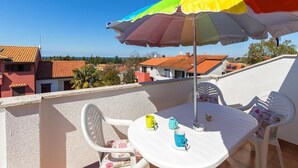 Un balcon avec une table et des chaises blanches, un parasol coloré et une vue sur les bâtiments en arrière-plan.