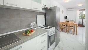 Une cuisine moderne avec des armoires blanches, un réfrigérateur en acier inoxydable, une cuisinière à gaz et un coin repas comprenant une table et des chaises en bois.