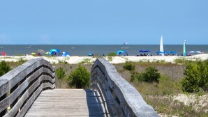 Un muelle de madera que conduce a una playa con sombrillas y gente.