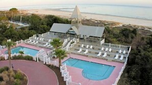 Un complejo turístico con dos piscinas, cancha de tenis y vistas a la playa.