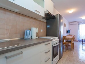 A modern kitchen with white cabinets, a built-in oven, a stainless steel refrigerator, and a coffee maker.