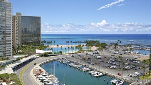 Un port de plaisance avec des bateaux, un parking et une plage bordée de palmiers.