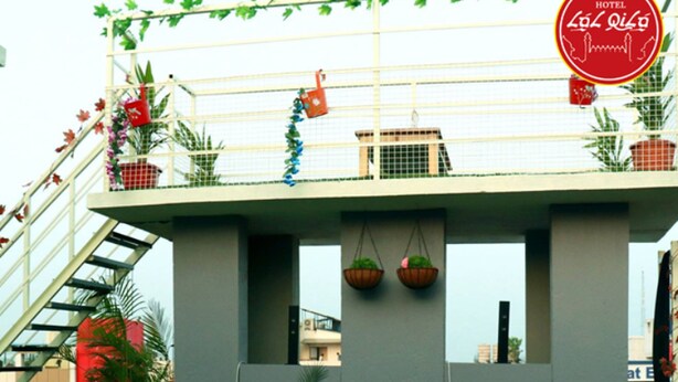 A hotel with a balcony decorated with plants and hanging baskets. There are potted plants on the ground and a staircase leading to the balcony. - Hotel Lal Qila (Bhubaneshwar)