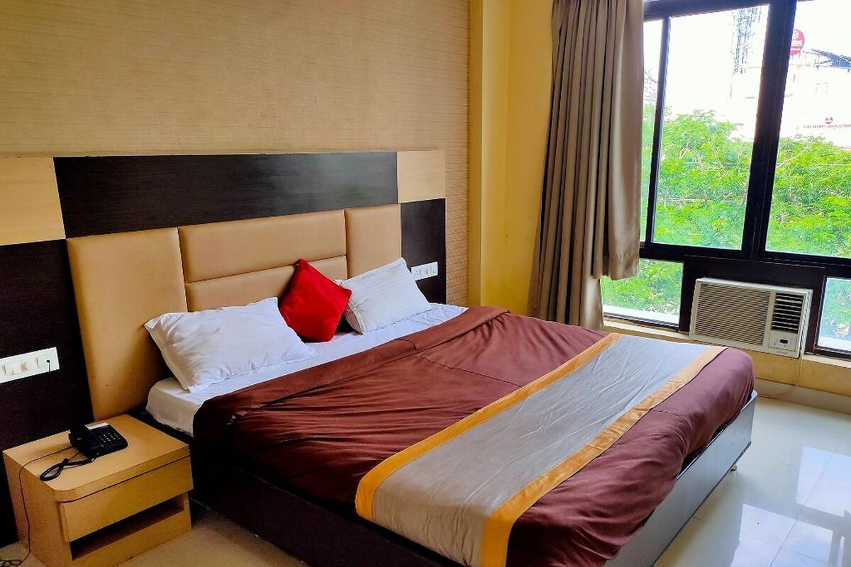A neatly made bed with a headboard, a bedside table with a phone, and a window with curtains.