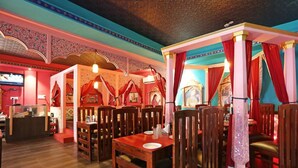 A restaurant with wooden tables and chairs, red curtains, and ornate wall decorations. - Hotel Lal Qila (Bhubaneshwar)