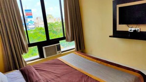 A hotel room with a bed, a TV mounted on the wall, and a window with curtains. - Hotel Lal Qila (Bhubaneshwar)