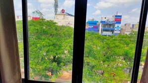A view through a window with greenery and buildings in the background, including a blue building with "Great Eastern" signage. - Hotel Lal Qila (Bhubaneshwar)