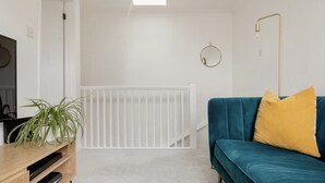 Un saló modern amb un sofà color turquesa, un coixí groc, una barana blanca i una làmpada al sostre.