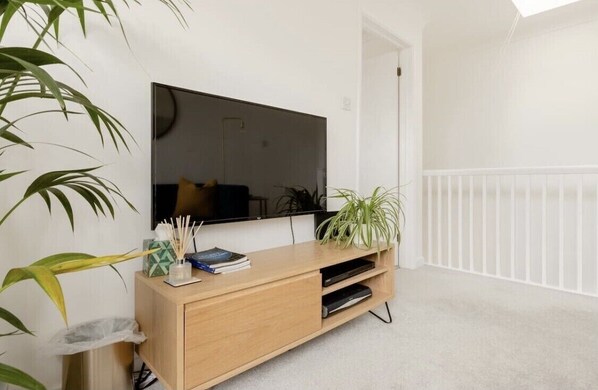 Una sala de estar moderna con un televisor de pantalla plana montado en la pared, un mueble de madera para entretenimiento y una barandilla blanca.