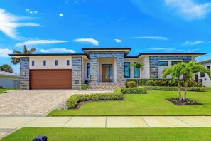 A modern two-story house with a stone facade, a large garage, and a well-maintained lawn. - Modern Home | Outdoor Kitchen & Steps to Beach (Marco Island)