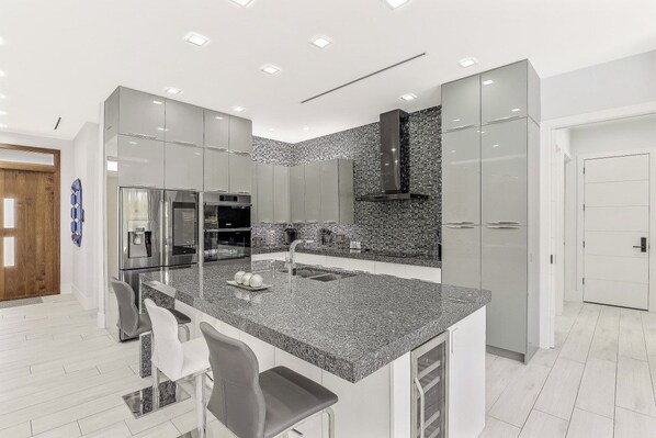A modern kitchen with a granite countertop, stainless steel appliances, and a large island with bar stools.