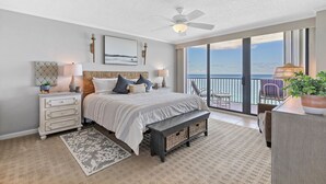 A bedroom with a large bed, bedside tables, a bench, a view of the ocean, and a balcony with chairs. - 🌊Breathtaking Ocean ViewsLuxury Penthouse-Daytona Ashley Penthouse 4🌊 (Daytona Beach Shores)