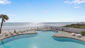 A pool with a curved edge, surrounded by lounge chairs and a palm tree, overlooking a beach. - 🌊Breathtaking Ocean ViewsLuxury Penthouse-Daytona Ashley Penthouse 4🌊 (Daytona Beach Shores)