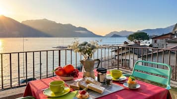 Ein Tisch mit Speisen und Getränken auf einem Balkon mit Blick auf einen See und Berge im Hintergrund.