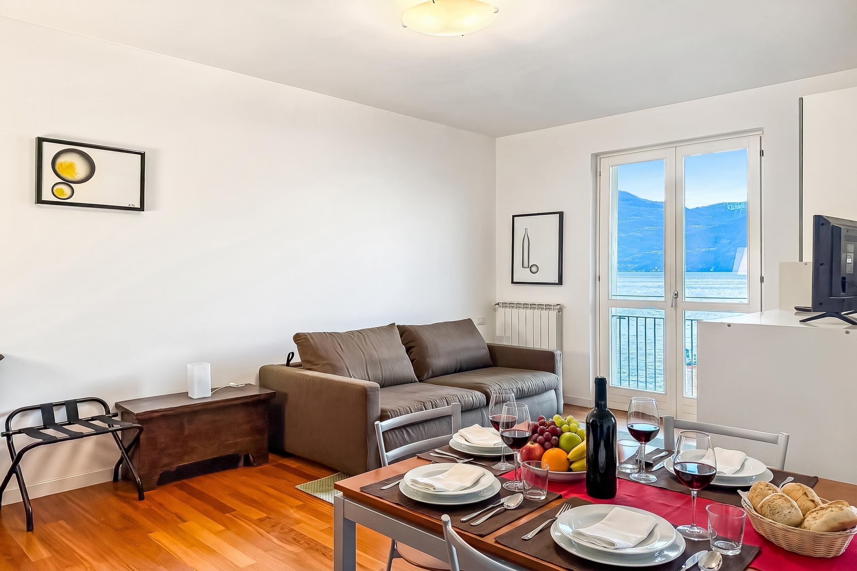Una sala moderna con sofá, mesa de comedor para dos personas y vista al mar a través de grandes ventanales.