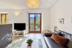 Una sala de estar moderna con un televisor de pantalla plana, un sofá, una mesa de centro con una planta y un ventanal con vistas a la vegetación.