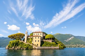 A historic building with a tower, situated on an island surrounded by water and mountains. - Lenno Centrale (Tremezzina)