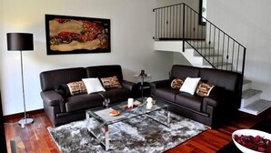 A living room with two black leather sofas, a glass coffee table, a painting on the wall, and a staircase. - Regina Grande (Laglio)