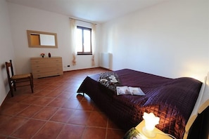 Quarto com cama, penteadeira, cadeira, janela e radiador.