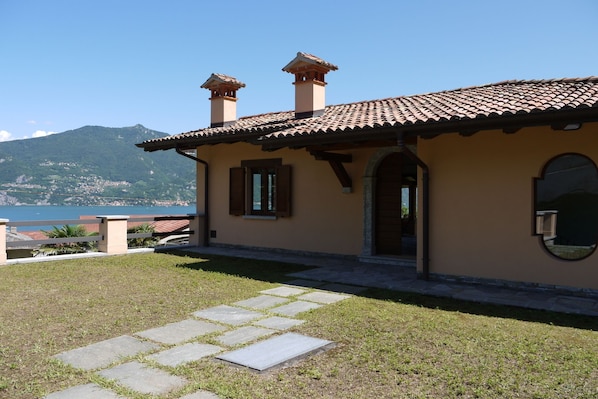 Uma casa com telhado de telhas, um caminho de pedra que leva à entrada e vista para um lago e montanhas ao fundo.