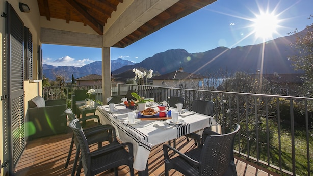 A balcony with a table set for dining, overlooking a mountainous landscape. - Villa Antico (Tremezzina)