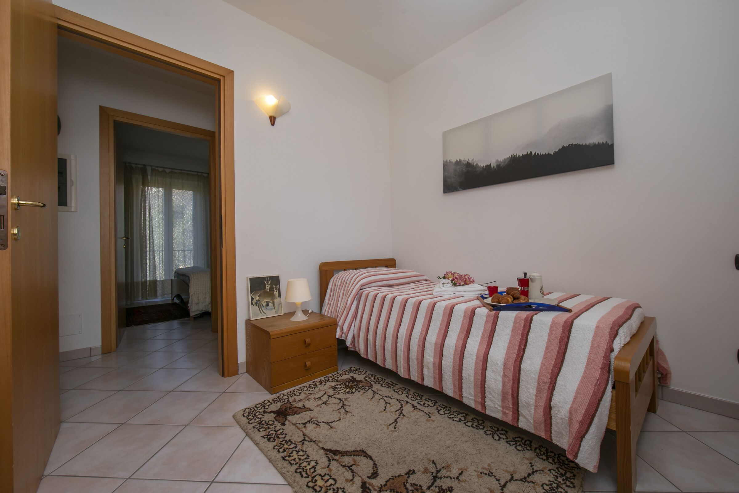 A bedroom with a bed, a nightstand, a lamp, a painting, and a rug.