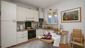 A compact kitchen with white cabinets, a microwave, and a sink. There's a dining table with a chair, a tray with croissants, and a potted plant. - Villa Antico (Tremezzina)