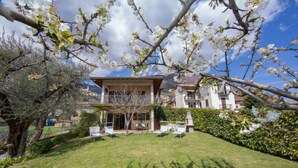 A two-story building with a balcony and a garden area with chairs. - Villa Antico (Tremezzina)