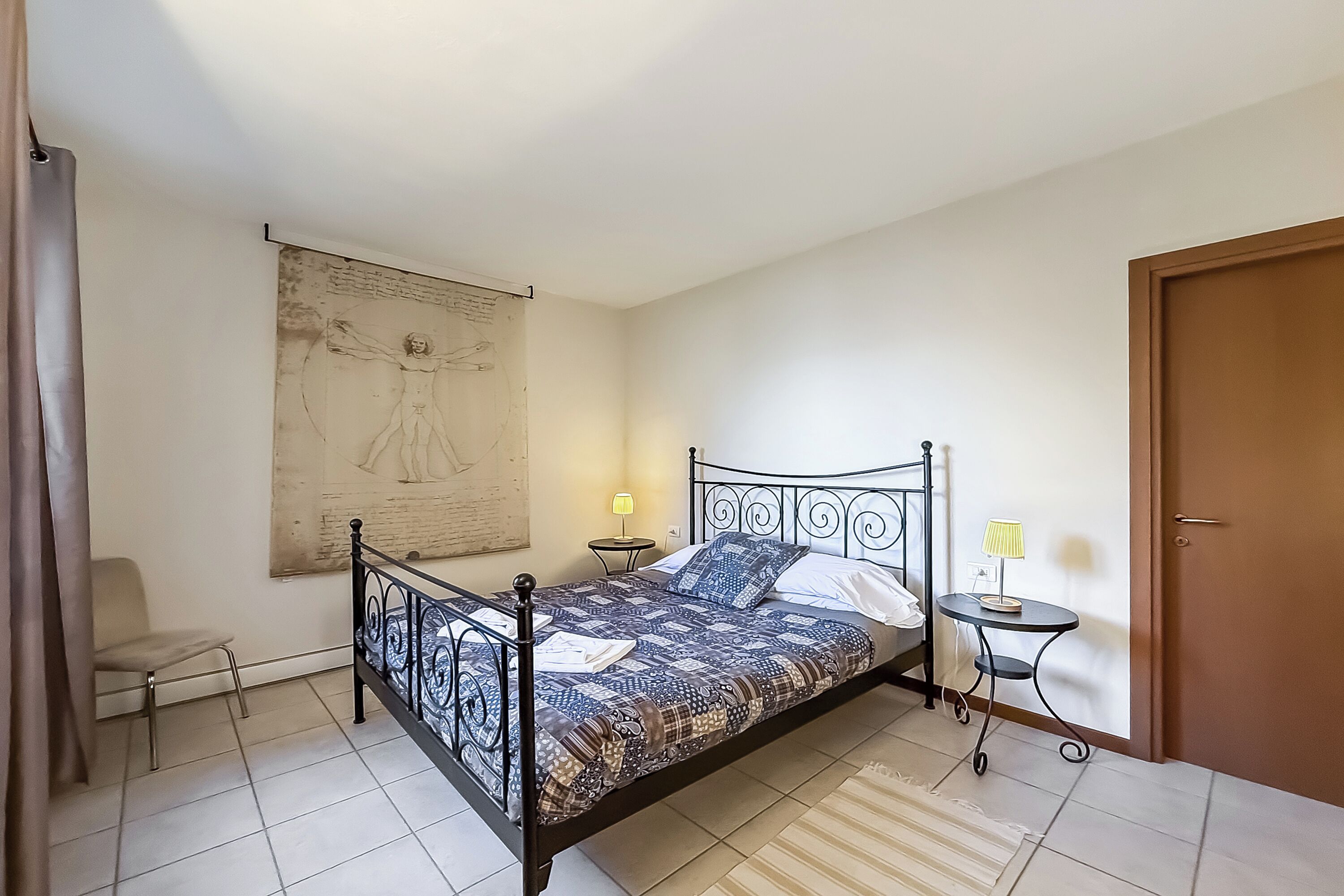 Une chambre à coucher avec un lit, une chaise, une petite table, une lampe et une porte.