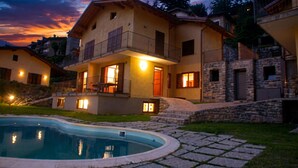 Una casa a due piani con piscina, facciata in pietra e un balcone con illuminazione esterna.