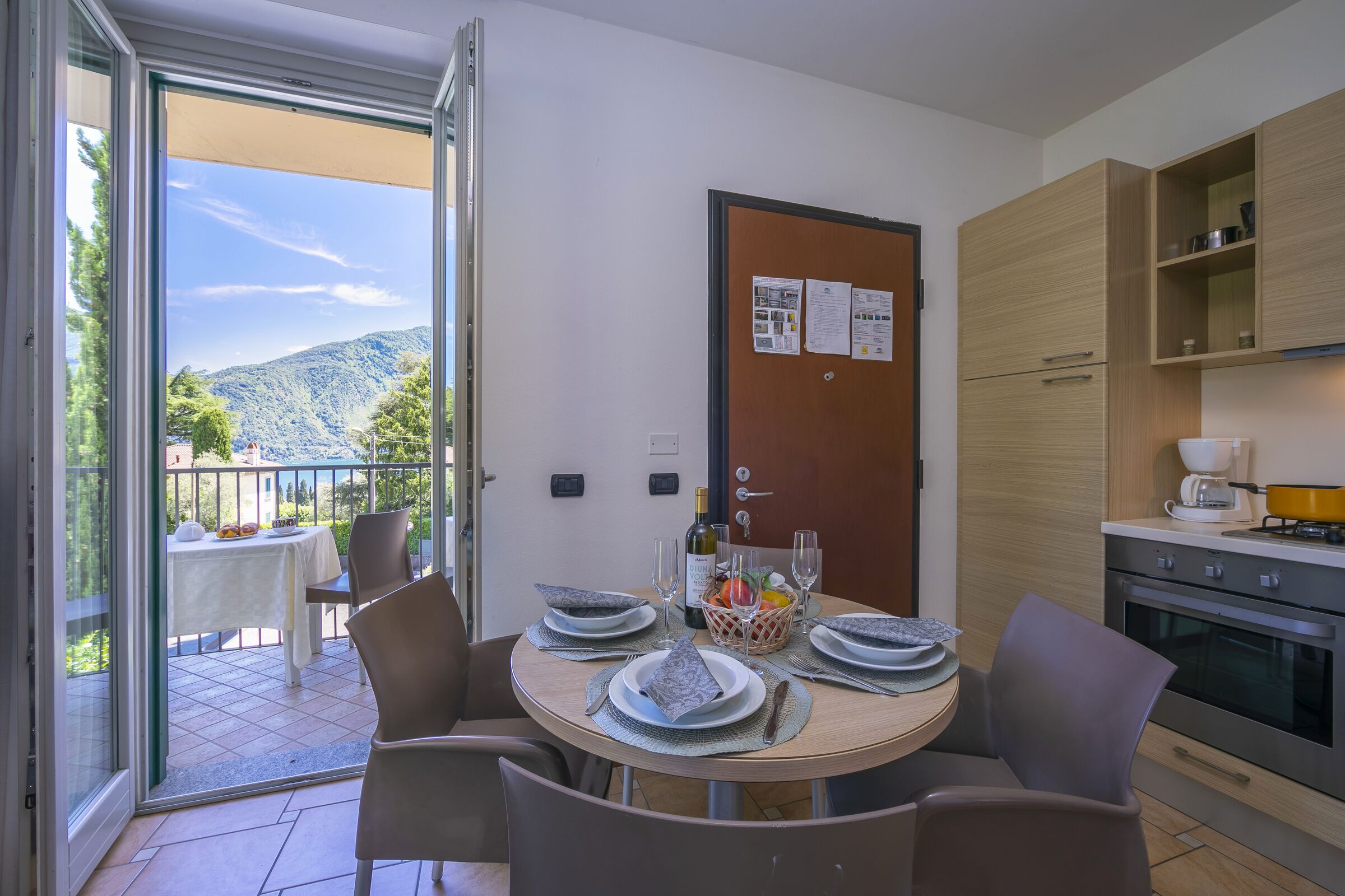 Un comedor con una mesa dispuesta para cuatro, una cocina equipada con electrodomésticos modernos y un balcón con vistas a la montaña.