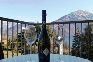 A bottle of wine and two glasses on a table with a mountain view in the background. - Belvedere Apt. 5 (Tremezzina)
