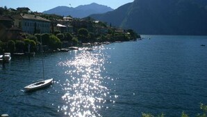 Ein See mit einem Boot, Gebäuden am Ufer und Bergen im Hintergrund.
