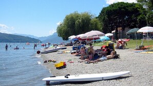 A pebbled beach with people, boats, and umbrellas. - Casa Monaco (Pianello del Lario)