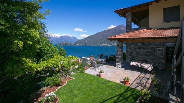A patio with outdoor furniture, a stone wall, and a view of a lake and mountains. - Casa Monaco (Pianello del Lario)
