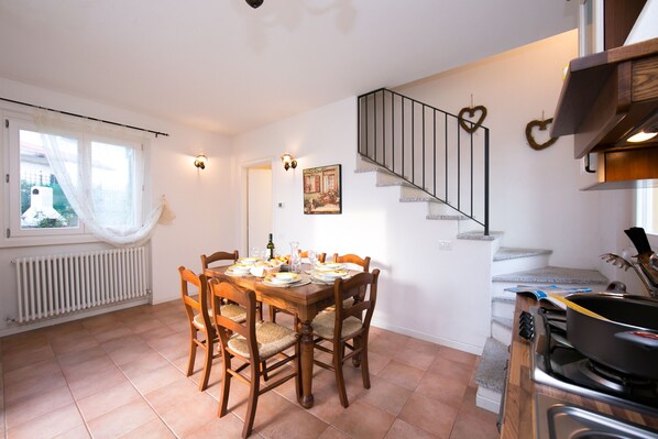 Un coin repas avec une table en bois dressée pour quatre personnes, un escalier avec une rampe en forme de cœur et un espace cuisine équipé d’une cuisinière et d’ustensiles.
