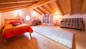 A bedroom with a wooden ceiling, a bed with a red blanket, a sofa, and a carpeted floor. - Casa Bella Juno (Gravedona)