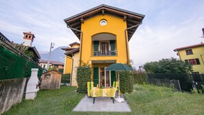 A yellow two-story house with a balcony, a small garden, and a green fence. - Casa Bella Juno (Gravedona)