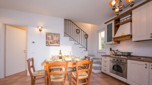A dining area with a wooden table and chairs, a staircase with heart-shaped decorations, and a kitchen with cabinets and a stove. - Casa Bella Juno (Gravedona)