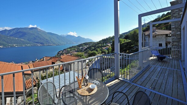 Ein Balkon mit Tisch für zwei Personen, mit Blick auf eine Berglandschaft und ein Gewässer.