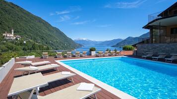 Una piscina con sillones de descanso, vista a un lago y montañas al fondo.