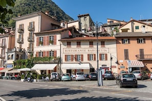 A street with parked cars, a restaurant named 'RISTORANTE BARCELLA,' and buildings with balconies. - Residence Eden Magnolia 13 (Argegno)
