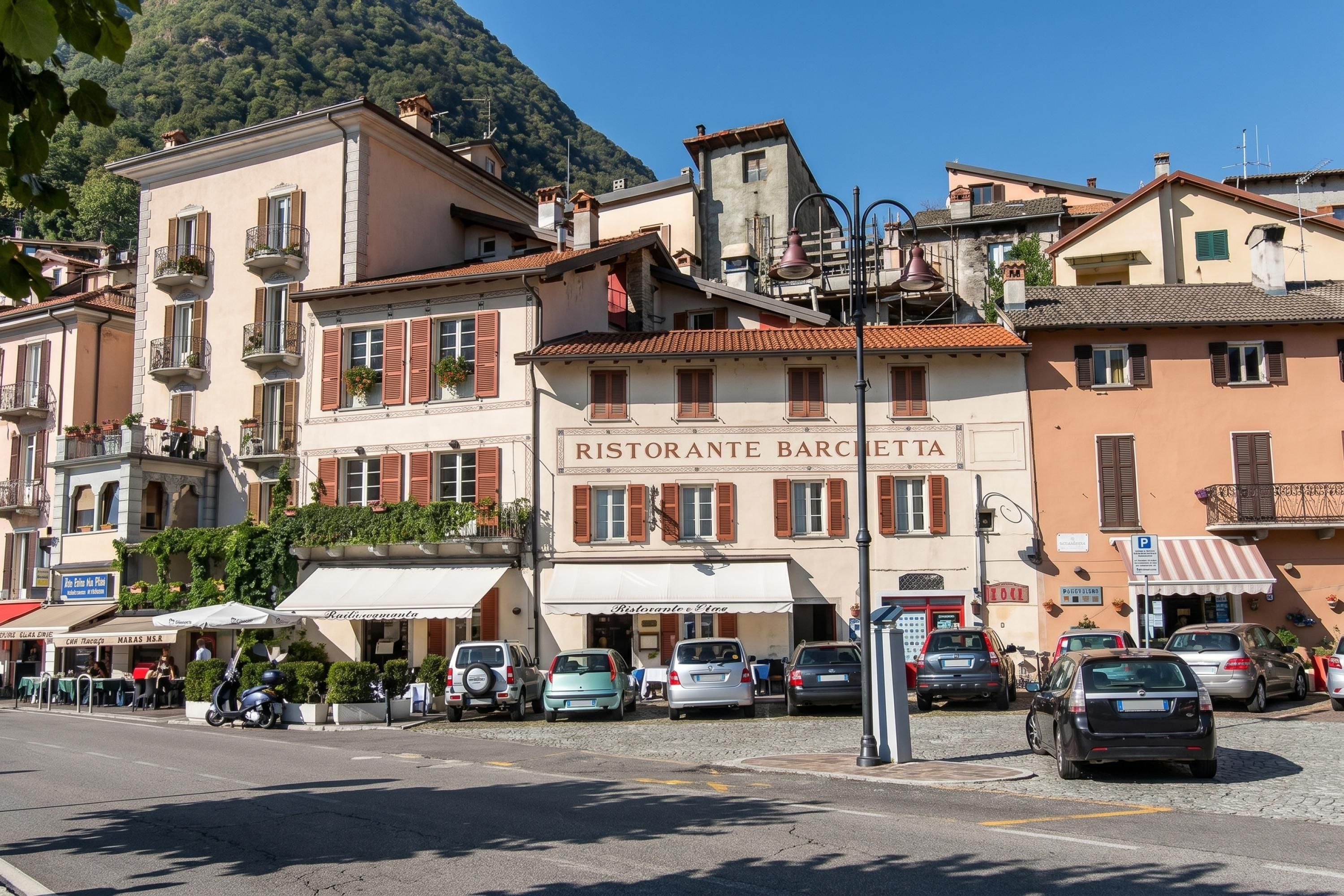 A street with parked cars, a restaurant named 'RISTORANTE BARCELLA,' and buildings with balconies.