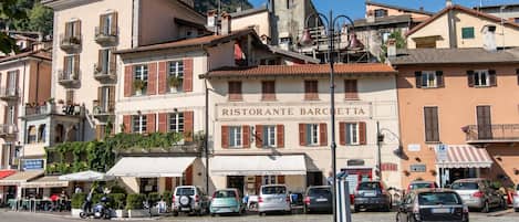 Eine Straße mit geparkten Autos, einem Restaurant namens 'RISTORANTE BARCELLA' und Gebäuden mit Balkonen.