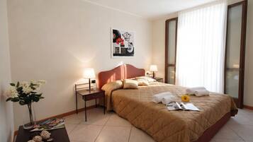 Habitación de hotel con cama, dos mesitas de noche, una lámpara de noche, un florero con flores, una revista y un cuadro en la pared.