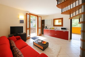 Una sala de estar moderna con un sofá rojo, un televisor de pantalla plana y una zona de cocina con armarios rojos y un microondas.
