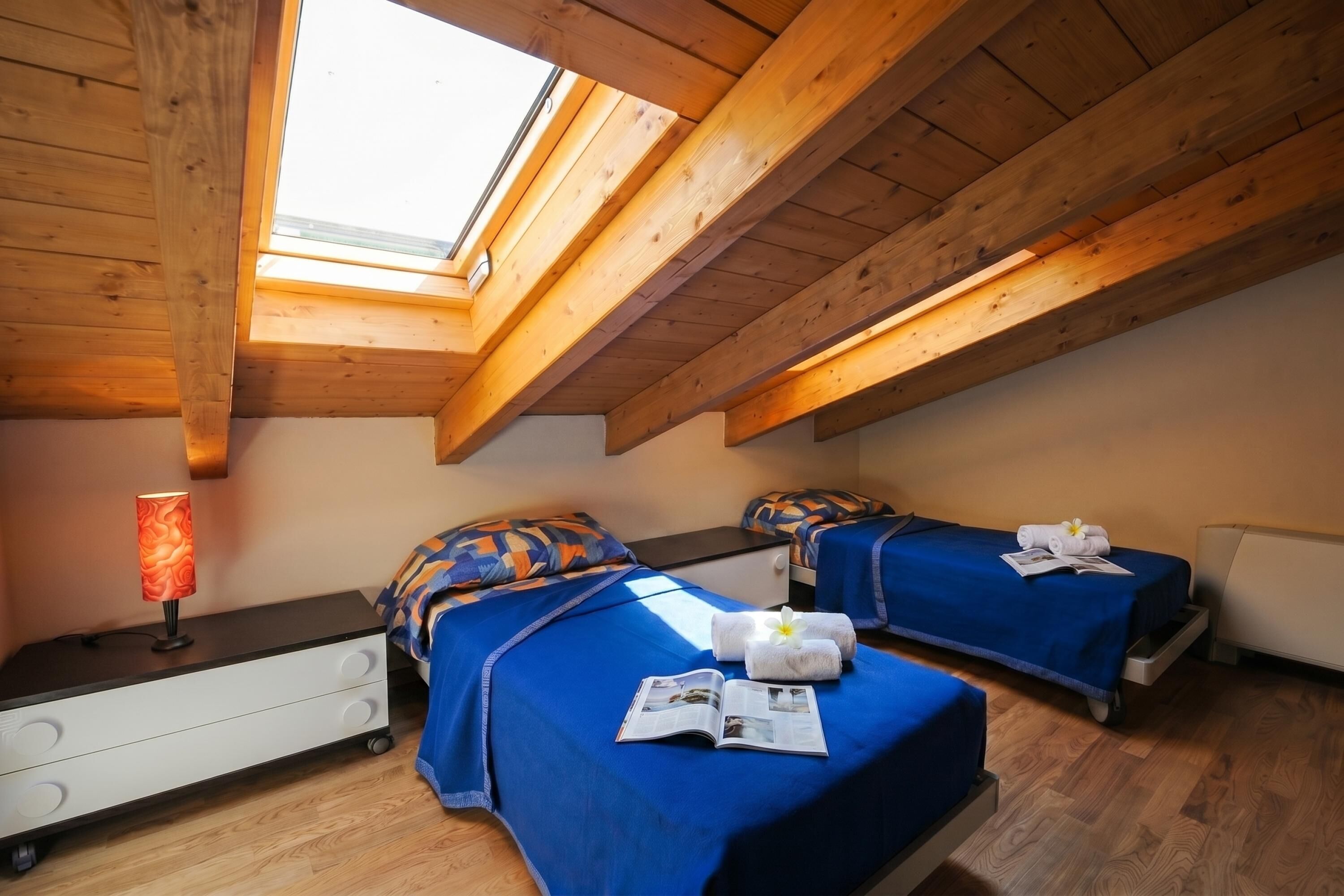 A room with two beds, a nightstand, a lamp, and a skylight.
