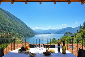 A table set outdoors with a scenic lake view, a bottle of wine, and various fruits and nuts.