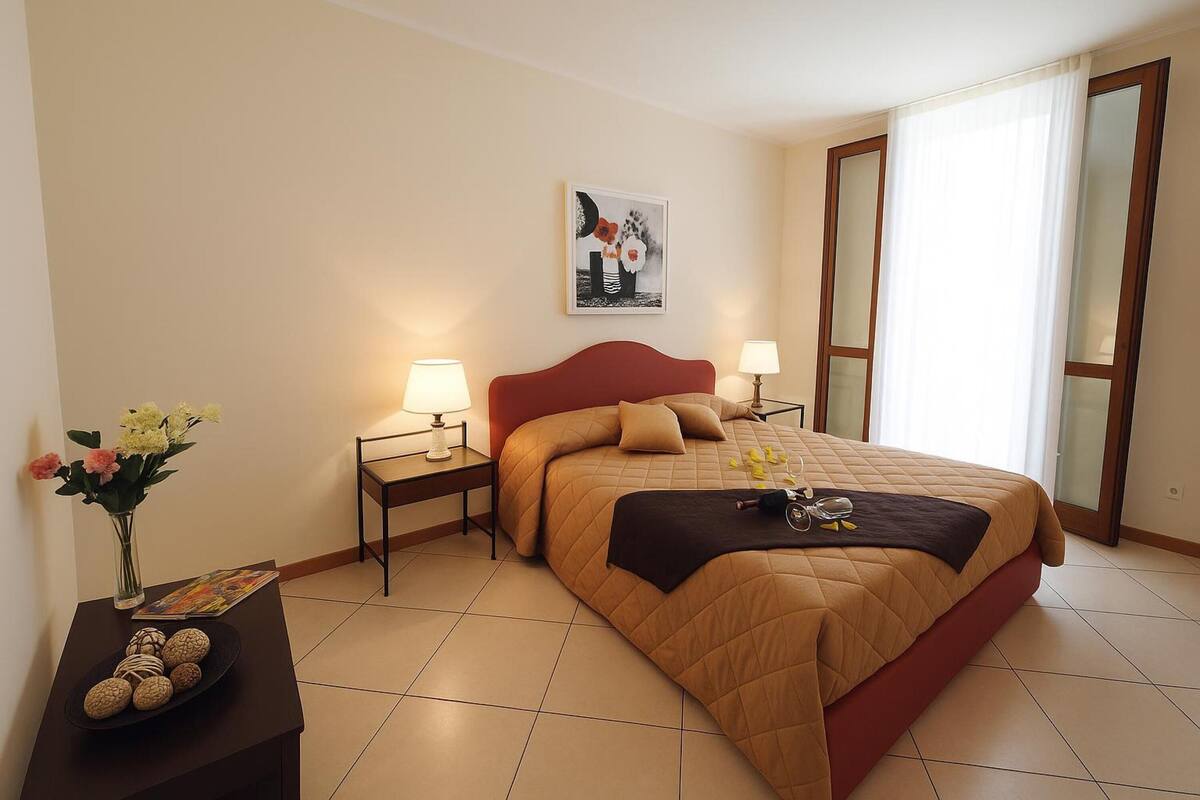 A neatly arranged hotel room with a bed, bedside tables, a vase of flowers, and a painting on the wall.