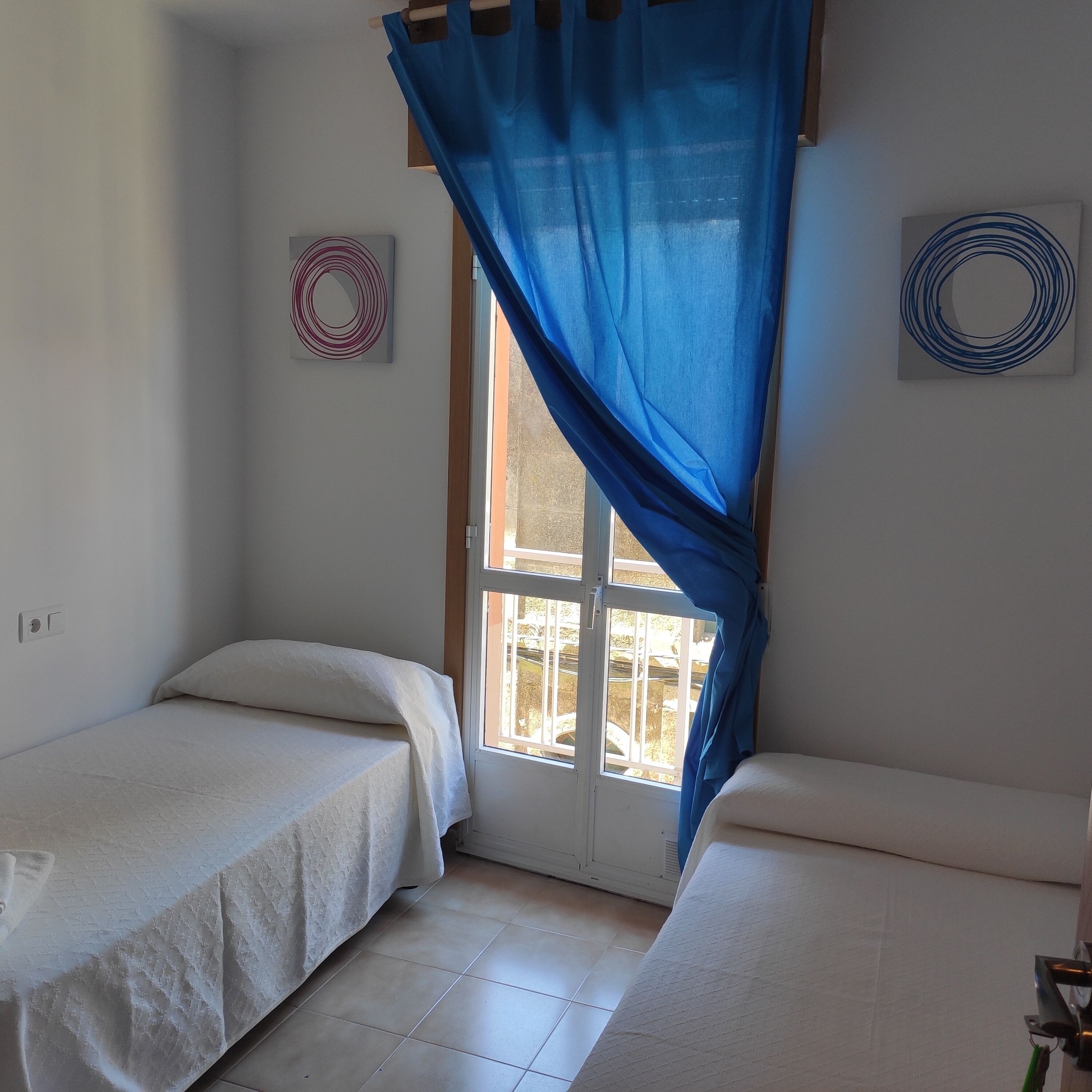 Una habitación con dos camas, una ventana con cortinas azules y dos adornos en la pared.